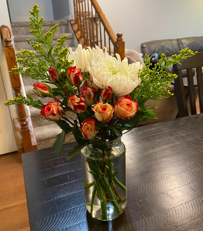 A glass mason jar with white mums, cream and red roses, and greenery.