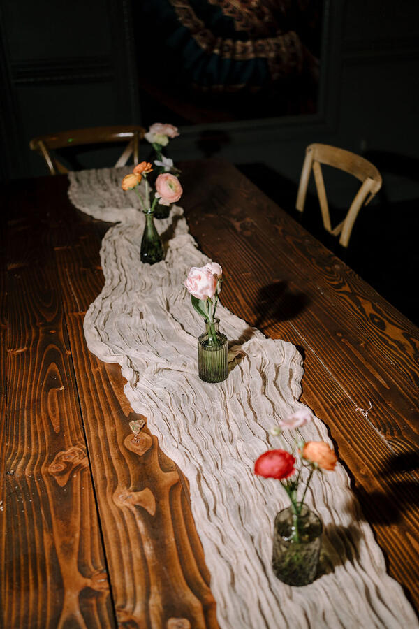 A table with a gauze tablecloth, and several small bud vases with peach and pink flowers.